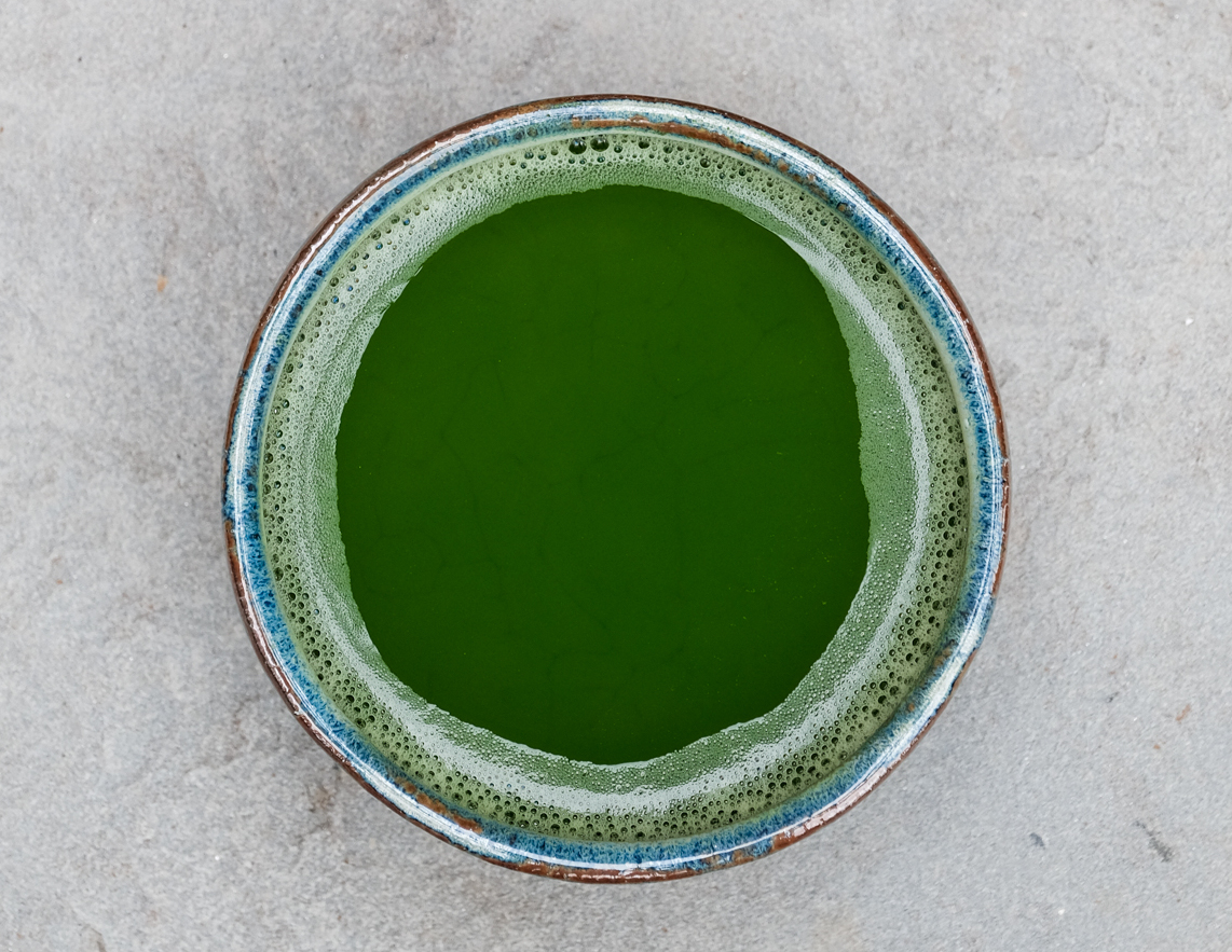 Bowl of freshly whisked ceremonial matcha seen from directly above, resting on stone