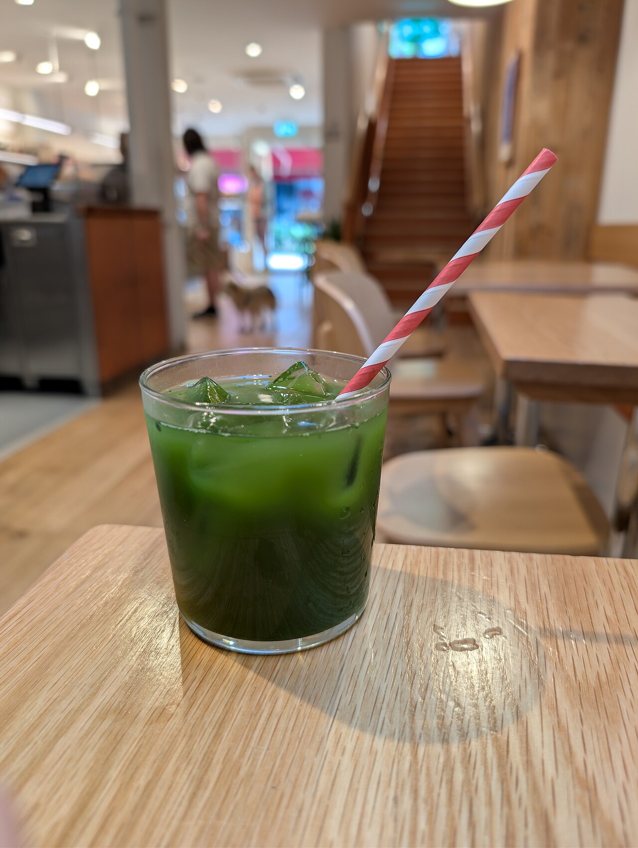 Glass of iced matcha over ice cubes with a paper straw on a wooden table