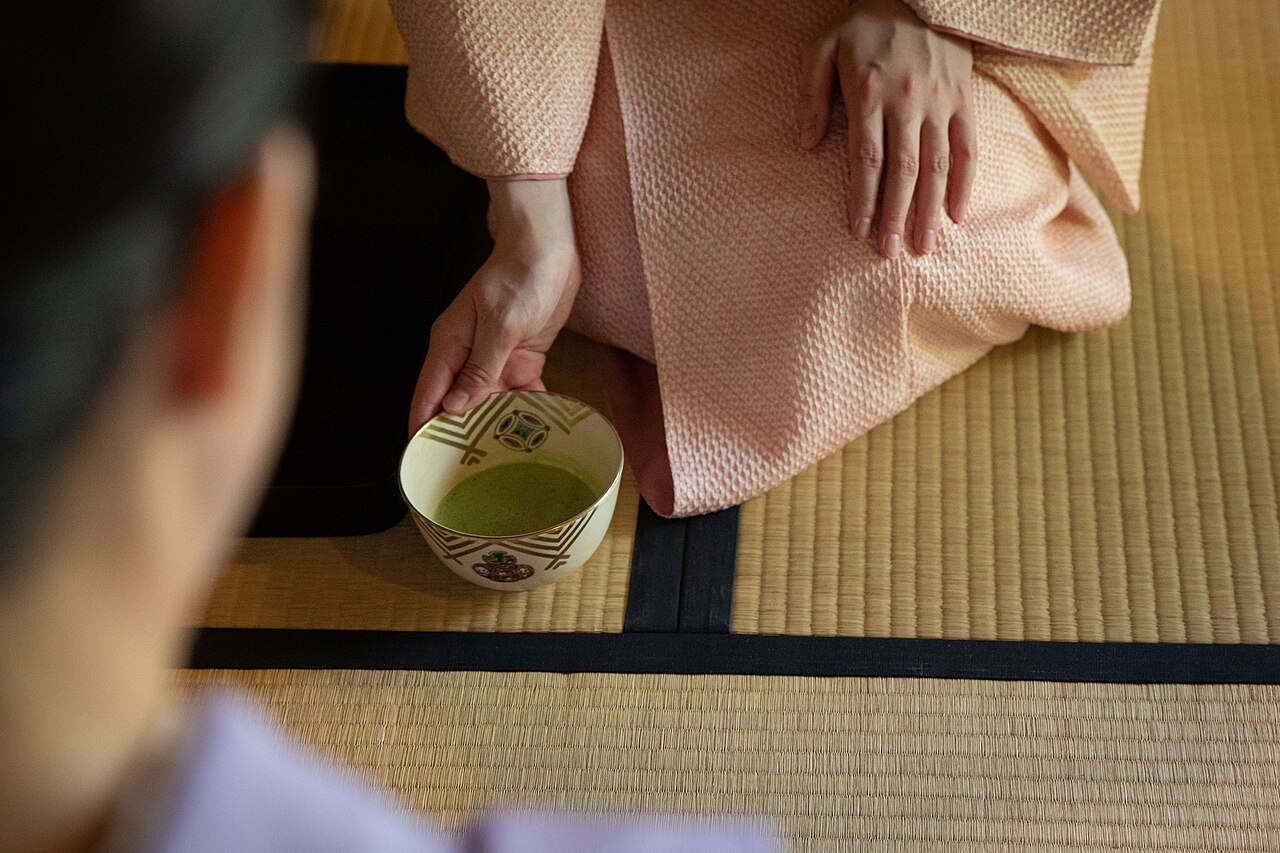 Host in a kimono setting down a bowl of matcha during a Japanese tea ceremony